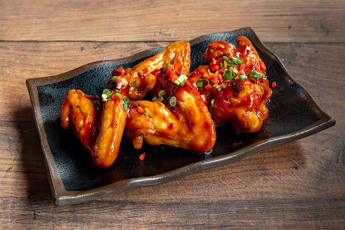 Spicy chicken wings on a black plate garnished with chopped green onions and red chili, symbolizing gifts with red flags.