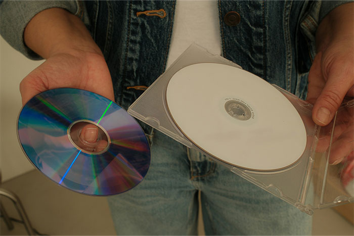 Person holding a blank CD and a clear CD case representing terrible gifts from partners and outdated presents.