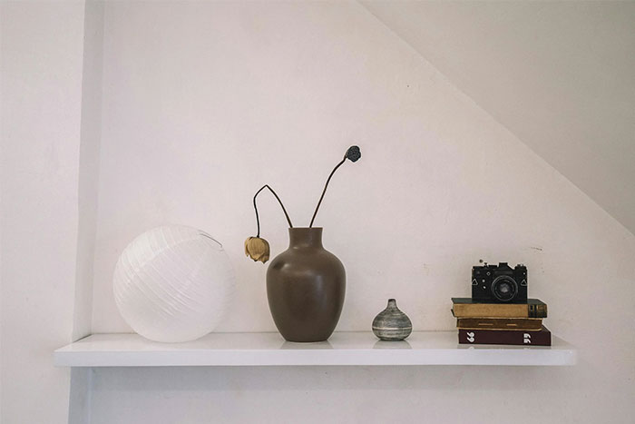 Minimalist white shelf with dried flowers in vases, vintage camera, and stacked books symbolizing gifts and relationship red flags.