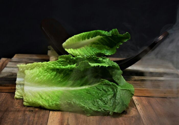 Fresh green lettuce leaves on a wooden surface, illustrating common foods that go bad more quickly than expected.