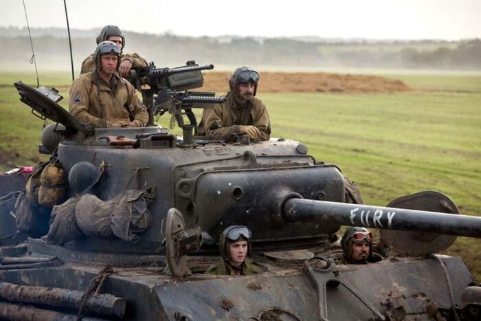 Actors in military gear on a tank set, showcasing behind-the-scenes moments from movies and TV productions.