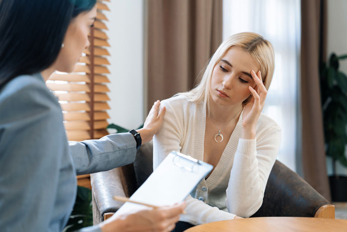 Couple seeking help with relationship struggles during a therapy session, woman looking upset while therapist offers support.