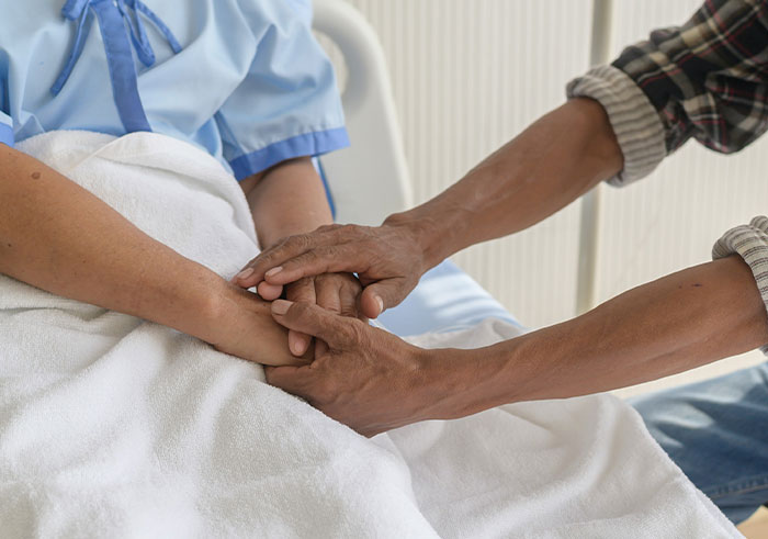 Patient lying in bed holding hands with a visitor, symbolizing support during life-changing moments that could destroy lives quickly