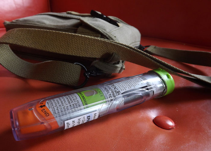 Epipen auto-injector and bag on red surface, illustrating emergency personnel equipment essentials.