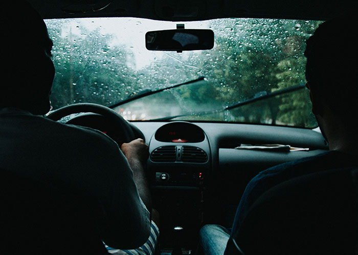 Two emergency personnel inside a vehicle driving in rainy weather, focused on the road ahead.