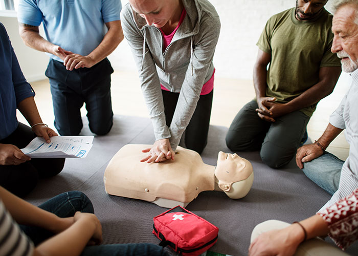 Group of people practicing CPR on a training mannequin during an emergency personnel safety and response class.