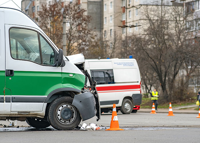 Damaged emergency vehicle at accident scene with personnel managing the situation and traffic cones in place