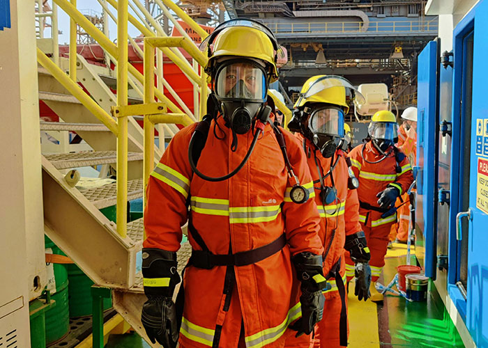 Emergency personnel in full protective gear and masks standing in an industrial setting during a safety drill.