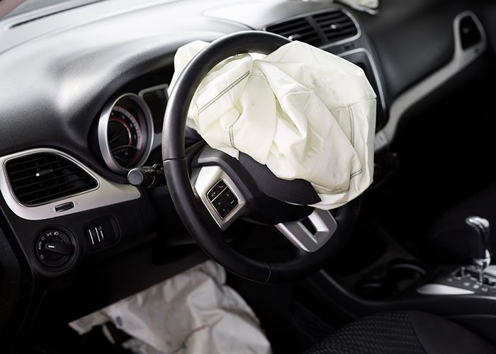 Deployed airbag on steering wheel inside damaged car, highlighting emergency personnel safety concerns.