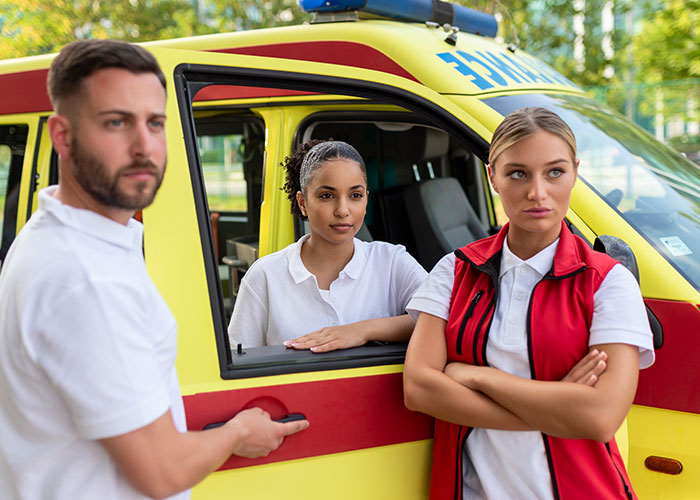 Three emergency personnel standing by a yellow ambulance, showing teamwork and readiness in an outdoor setting.