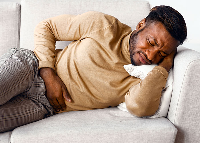 Man lying on a couch in pain holding his abdomen, illustrating emergency personnel advice on urgent health concerns.