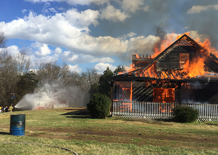 House engulfed in flames with firefighters spraying water, illustrating important emergency personnel safety tips.