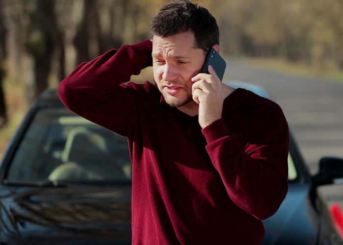 Man in a red sweater making an urgent call near a car, illustrating emergency personnel safety and response tips.