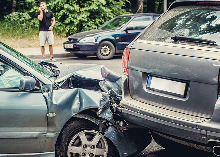 Two cars damaged in a collision with a man on phone in the background, highlighting emergency personnel insights.