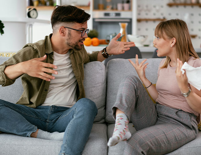 Man and woman having a heated conversation on a couch, illustrating experiences that made people say never doing that again.