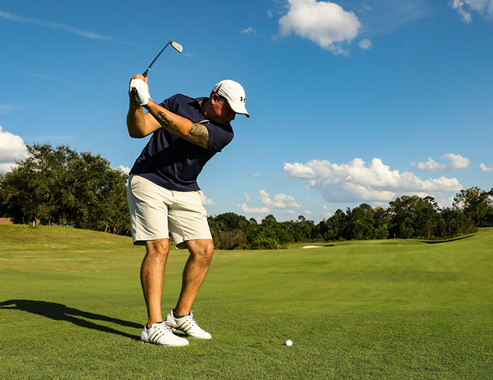 Man preparing to golf swing on a sunny golf course, one of the experiences that made people say never doing that again.