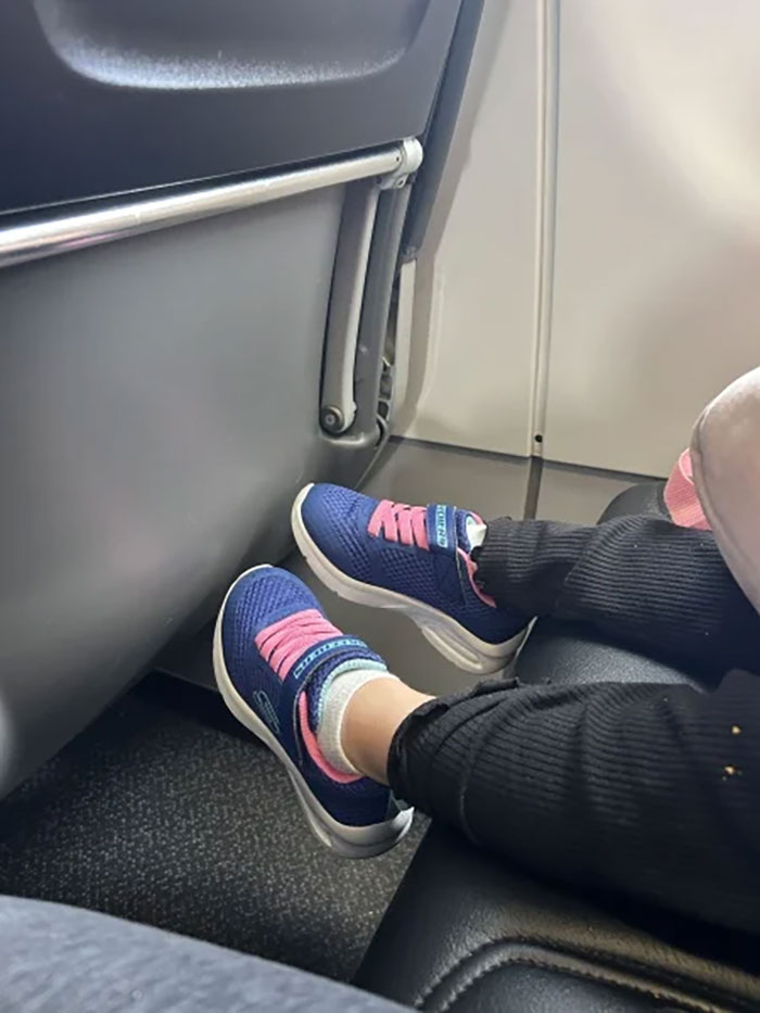 Toddler wearing blue and pink shoes fidgeting on an airplane seat during a mid-flight mom defense incident. Toddler wearing blue and pink shoes fidgeting on an airplane seat during a mid-flight mom defense incident.
