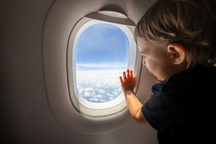 Toddler looking out airplane window mid-flight, captured during a mom defending child from angry passenger over fidgeting. Toddler looking out airplane window mid-flight, captured during a mom defending child from angry passenger over fidgeting.
