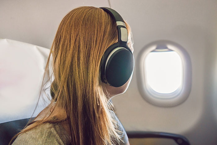 Mom wearing headphones looking out airplane window, defending toddler during mid-flight passenger conflict over fidgeting. Mom wearing headphones looking out airplane window, defending toddler during mid-flight passenger conflict over fidgeting.