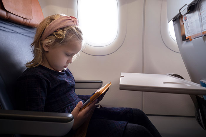 Toddler sitting quietly on airplane seat playing with tablet as mom defends her mid-flight amid passenger fidgeting dispute. Toddler sitting quietly on airplane seat playing with tablet as mom defends her mid-flight amid passenger fidgeting dispute.