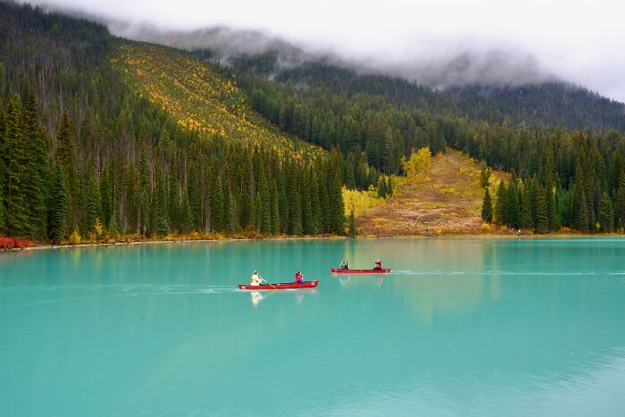 Three people canoeing on a turquoise lake surrounded by forested mountains, showcasing natural wonders full of magic.