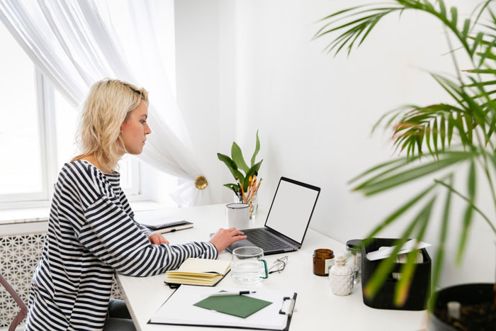 Woman working quietly on laptop in a bright room, reflecting on jobless partner&rsquo;s anger and toxic home environment.