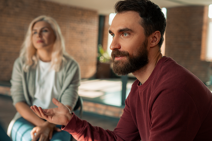 Man with beard discussing seriously with a woman in a casual setting about uninviting parents from brother&rsquo;s wedding.
