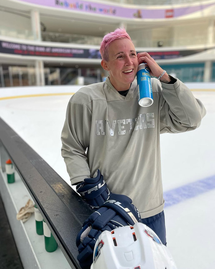 Female athlete in hockey gear smiling on ice rink, holding water bottle after restroom mistake by female attendant.