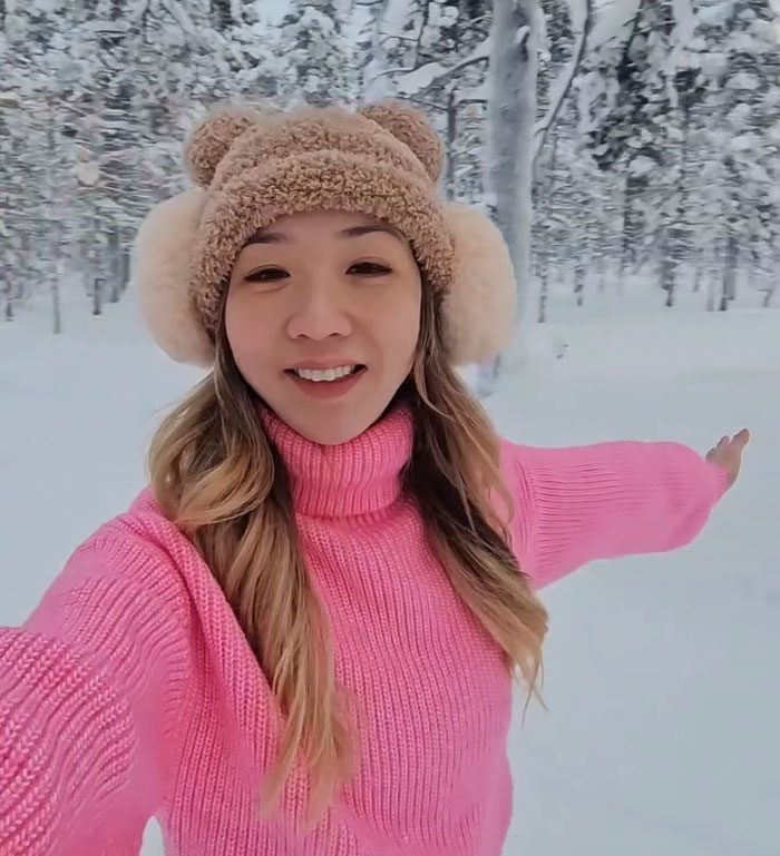 Travel expert wearing pink sweater and winter hat takes selfie in snowy forest sharing her top tip for best plane seat timing. Travel expert wearing pink sweater and winter hat takes selfie in snowy forest sharing her top tip for best plane seat timing.