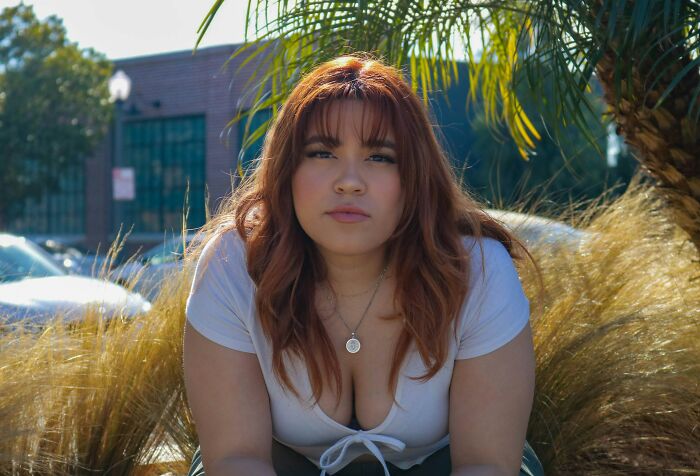 Young woman with red hair sitting outdoors, reflecting the most soul-crushing things parents ever told them