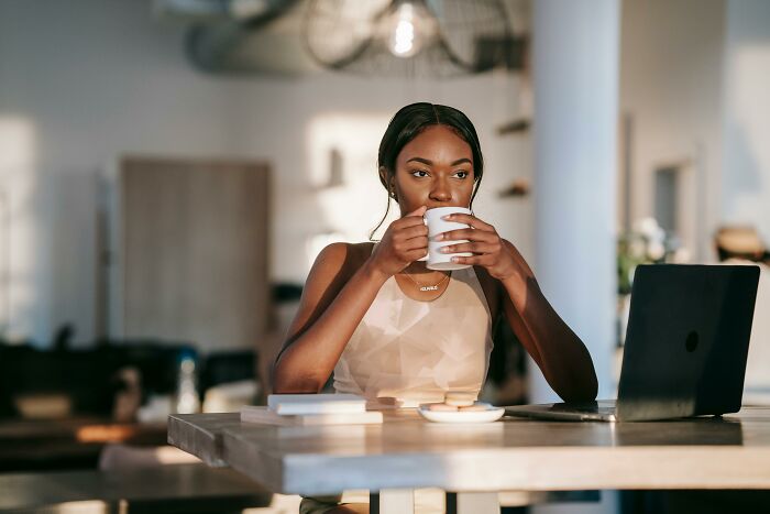 Young woman drinking coffee at a table with laptop, reflecting on examples of incredibly unhealthy things people do.