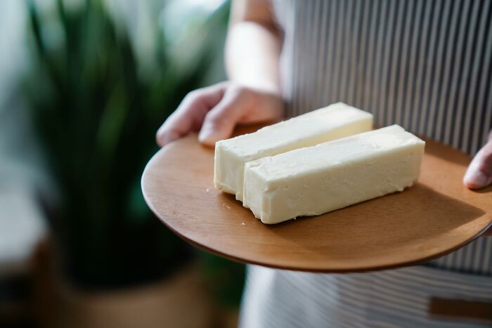 Person holding a wooden plate with two large blocks of unhealthy processed cheese, illustrating unhealthy things people do.