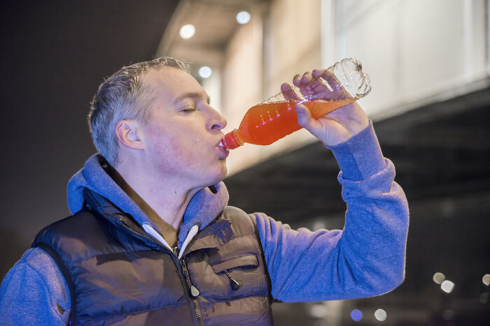 Man drinking orange soda outdoors at night illustrating examples of incredibly unhealthy things people do.