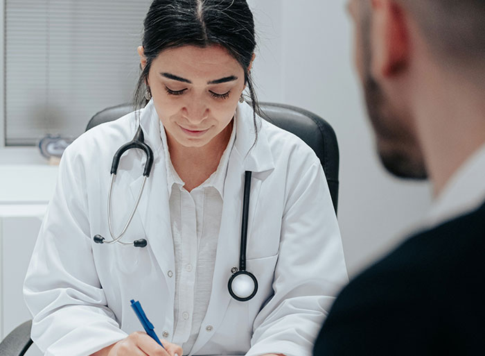 Healthcare worker in white coat with stethoscope writing notes during patient consultation in clinical setting