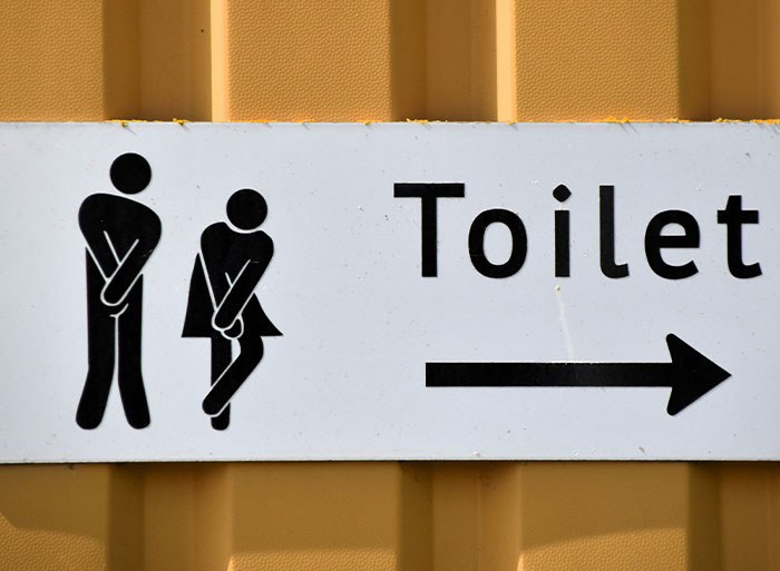 Sign showing two figures needing a toilet with an arrow, illustrating wild analogies healthcare workers use for medical problems.