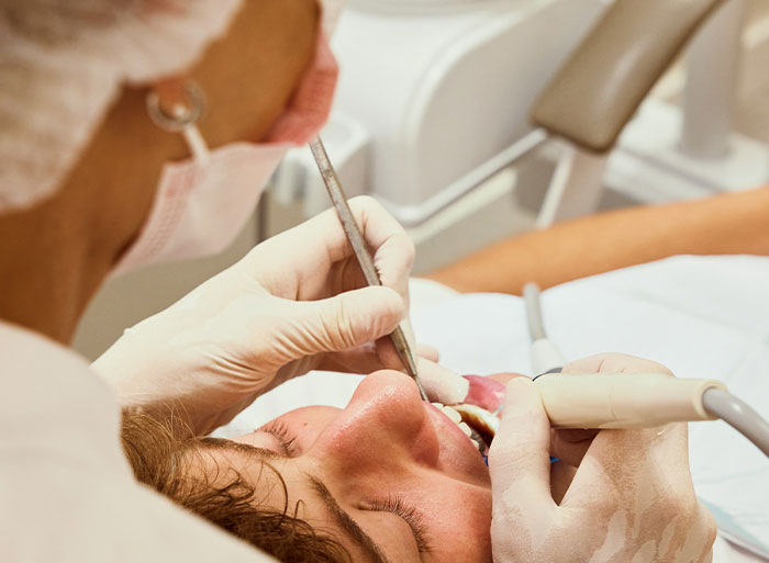 Healthcare worker wearing gloves treating a patient's dental issue using medical tools in a clinical setting.