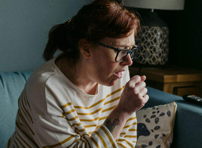 Woman with glasses coughing into hand, illustrating healthcare workers using wild analogies to explain medical problems.