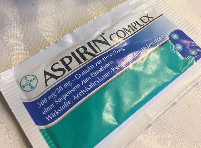 Packet of Aspirin Complex medication lying on a white textured surface, related to healthcare workers and medical problems.