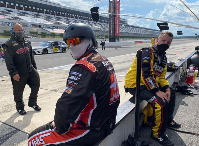 Three masked healthcare workers wearing racing suits at a pit stop, illustrating wild analogies to explain medical problems.