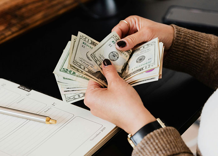 Hands counting US dollar bills over an open planner, representing unknowingly paying rent to husband and his mom.