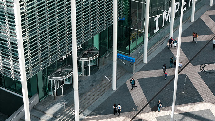 Aerial view of people walking outside a modern building with large pillars and the word Imperial on the facade.