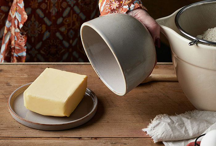Person holding a bowl near butter and a colander in a kitchen setting with common cooking advice items visible