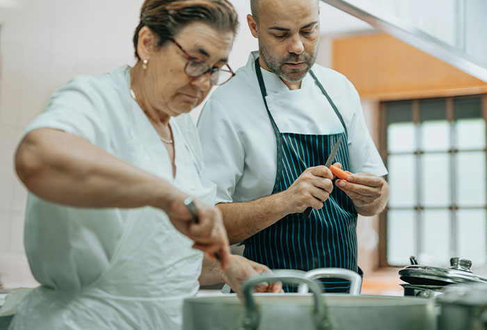 Two chefs in a kitchen, one peeling a carrot and the other stirring a pot, sharing common cooking advice.
