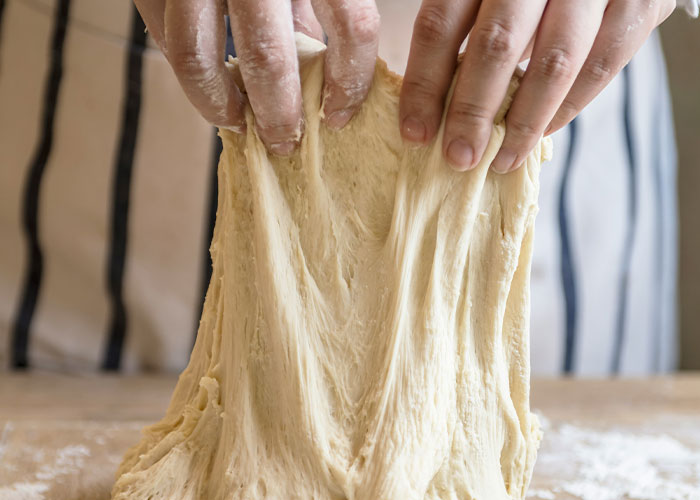 Hands stretching sticky dough over a floured surface illustrating common cooking advice that doesn’t really work.