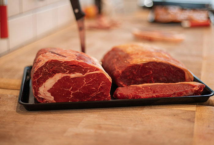 Raw steaks on a black tray on a wooden kitchen counter, illustrating common cooking advice that doesn’t really do anything.