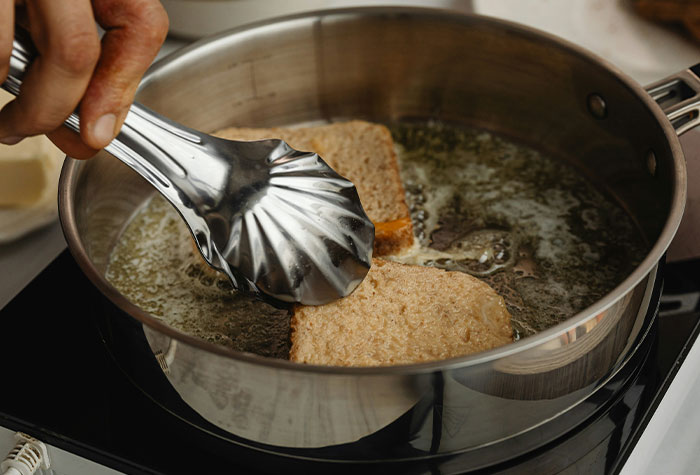 Person using metal tongs to cook bread slices in hot oil on stovetop, illustrating common cooking advice.
