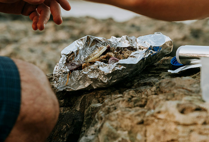 Hands preparing food wrapped in foil on a rock, illustrating common cooking advice shared by people outdoors.