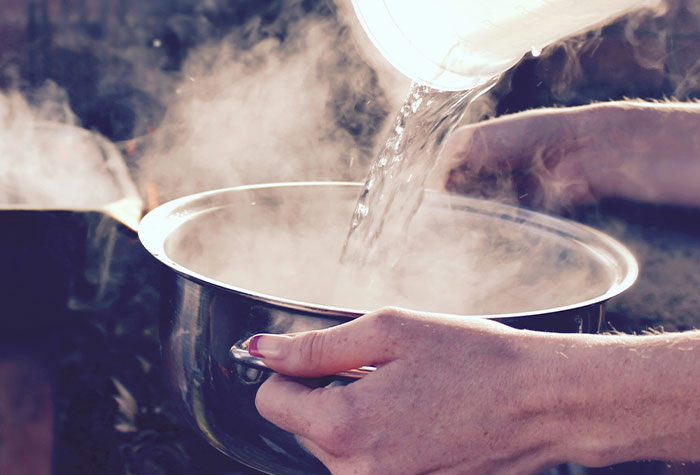Pouring water into a steaming pot with hands visible, illustrating common cooking advice and kitchen practices.