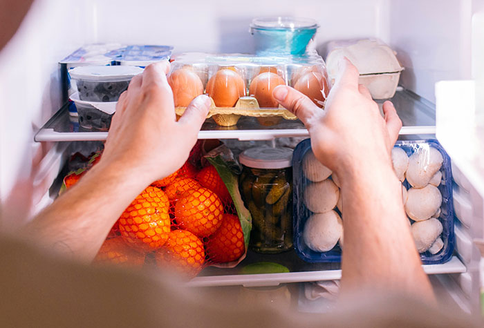 Hands placing eggs in a refrigerator filled with fruits, vegetables, and other common cooking ingredients.