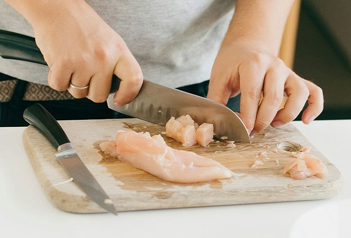 Person chopping raw chicken on a wooden board, demonstrating common cooking advice shared by many home cooks.